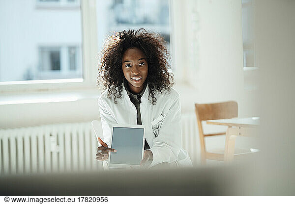 Smiling female doctor with curly hair pointing at tablet PC
