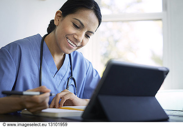 Smiling female doctor writing on diary while working at desk in hospital