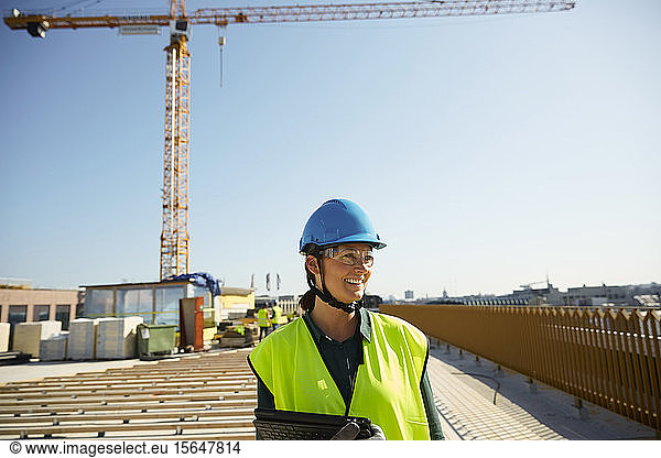 Smiling female engineer in reflective clothing with digital tablet at construction site against clear sky