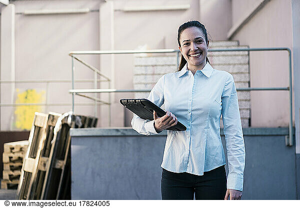 Smiling female engineer standing with tablet PC at factory