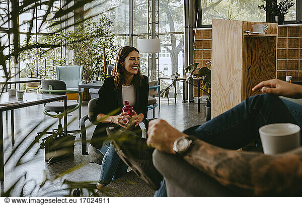 Smiling female entrepreneur discussing with male colleague during coffee break at coworking office
