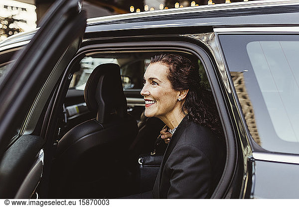 Smiling female entrepreneur looking away while exiting from car