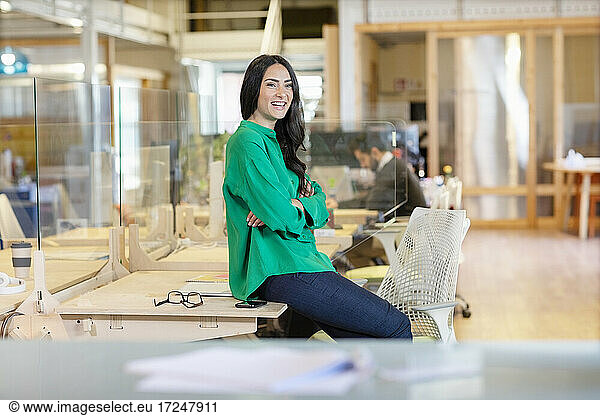 Smiling female entrepreneur looking away while sitting on desk in office