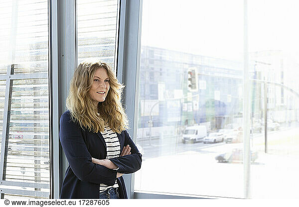 Smiling female entrepreneur looking away while standing in front of glass window in office