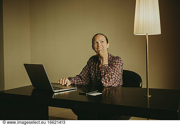 Smiling female entrepreneur looking away while working on laptop in office