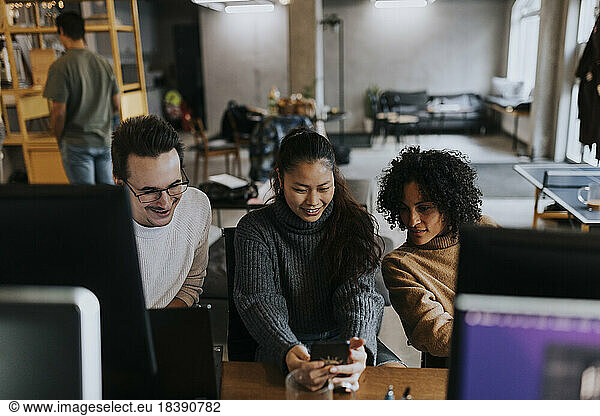 Smiling female entrepreneur sharing smart phone with colleagues in startup company