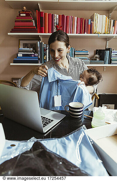 Smiling female entrepreneur showing shirt on video call through laptop while working at home office