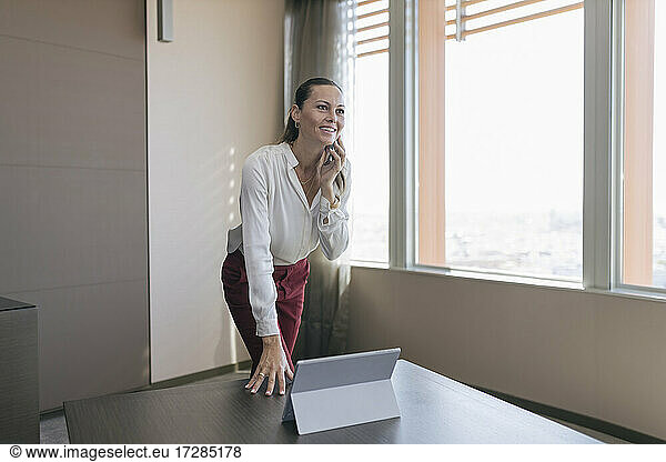 Smiling female entrepreneur talking on mobile phone at desk in office