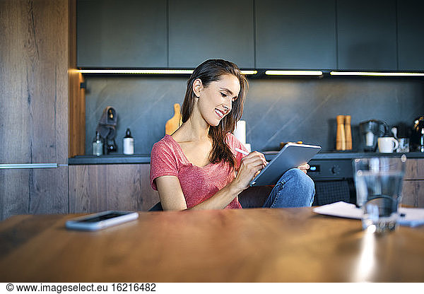 Smiling female entrepreneur using digital tablet while sitting at desk in home office