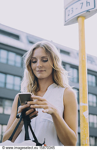 Smiling female entrepreneur using smart phone against building in city