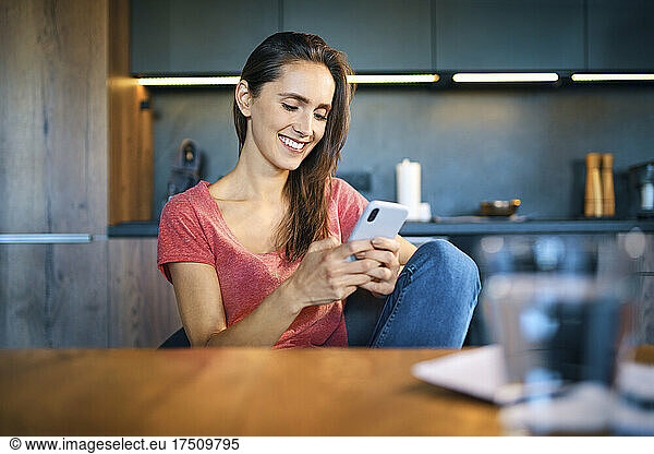 Smiling female entrepreneur using smart phone while sitting at desk in home office