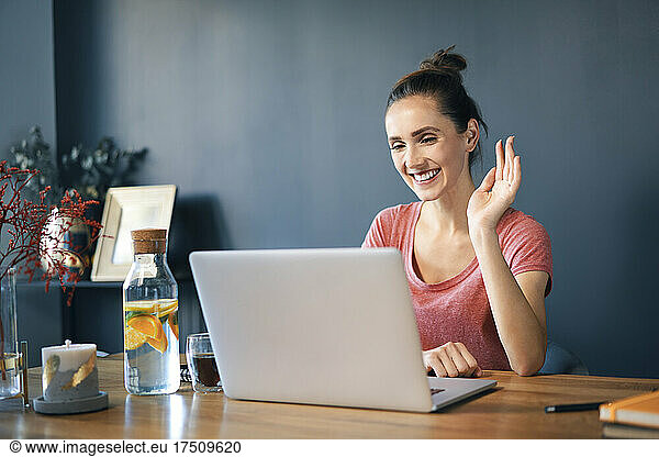 Smiling female entrepreneur video conferencing over laptop on desk in home office