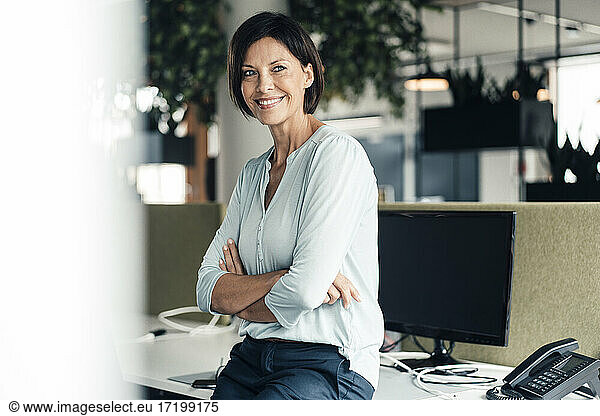 Smiling female entrepreneur with arms crossed against computer in office