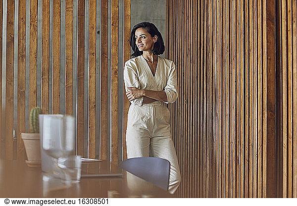 Smiling female entrepreneur with arms crossed standing against wooden doors in office