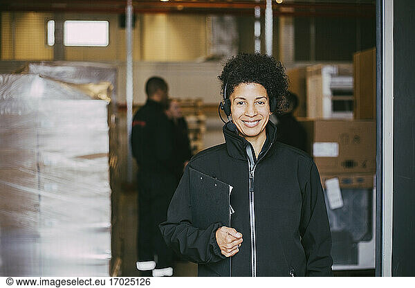 Smiling female entrepreneur with clipboard at warehouse