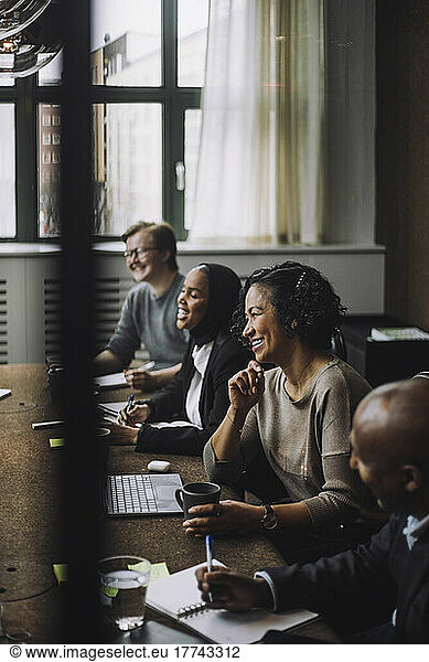 Smiling female entrepreneur with hand on chin sitting by colleagues at conference table