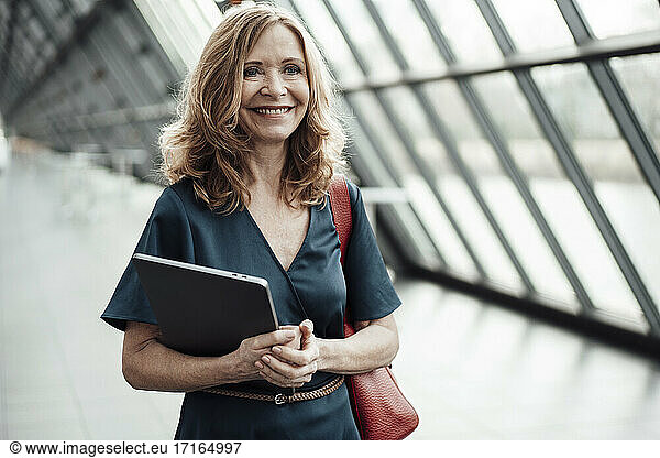 Smiling female entrepreneur with laptop in office corridor