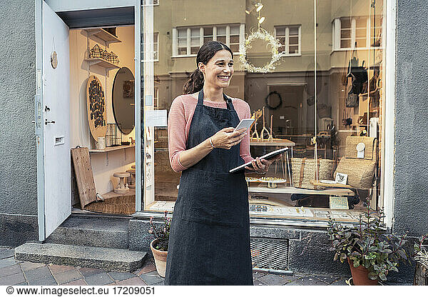 Smiling female entrepreneur with smart phone and digital tablet outside store