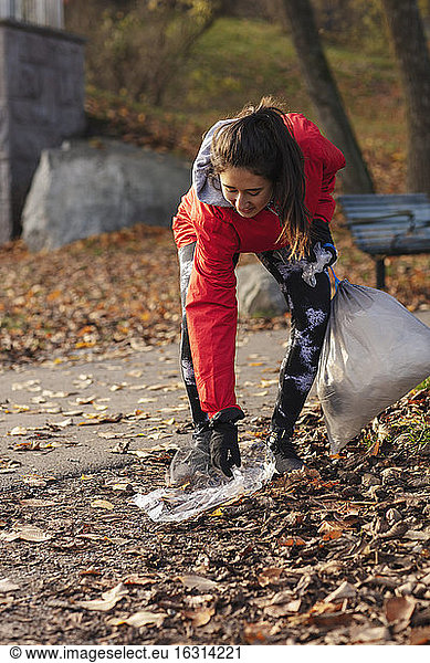 Smiling female environmentalist collecting plastic waste in park during autumn