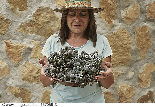 Smiling female farmer holding grapes while standing