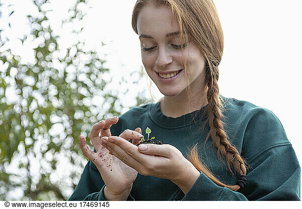 Smiling female farmer with braided hair touching plant in hand