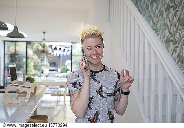 Smiling female freelancer talking on smart phone in kitchen