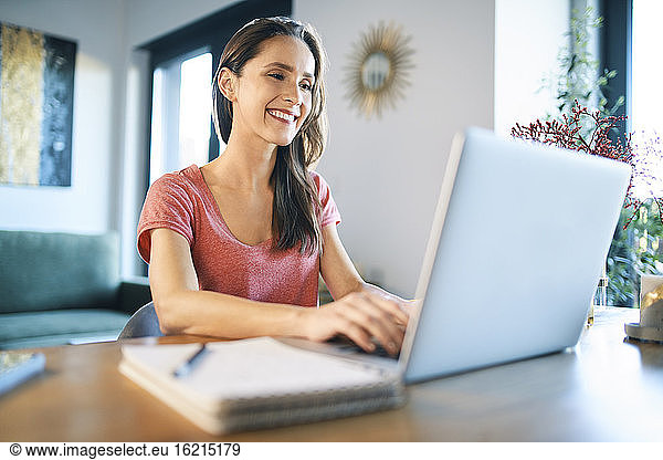Smiling female freelancer using laptop on desk in home office
