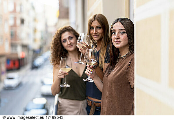 Smiling female friends holding wineglasses standing on balcony