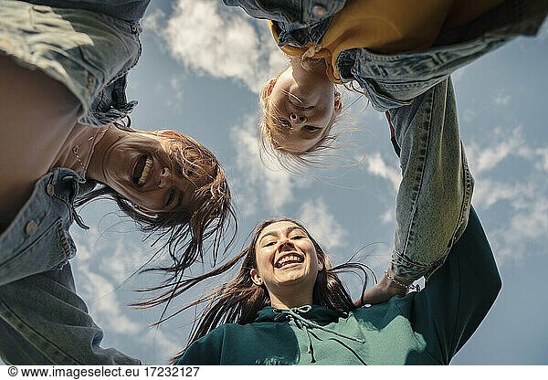 Smiling female friends looking down against sky on sunny day