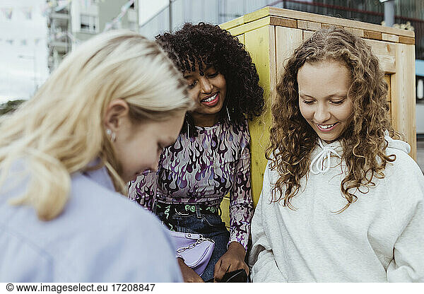 Smiling female friends looking down by box container outdoors