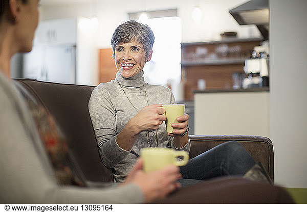 Smiling female friends talking while sitting on sofa at home