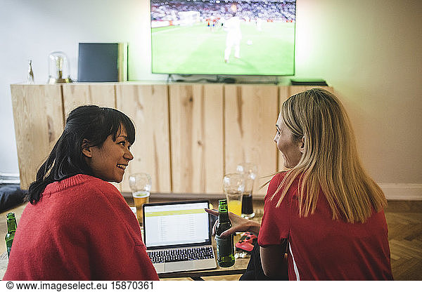 Smiling female friends talking while watching soccer match at home