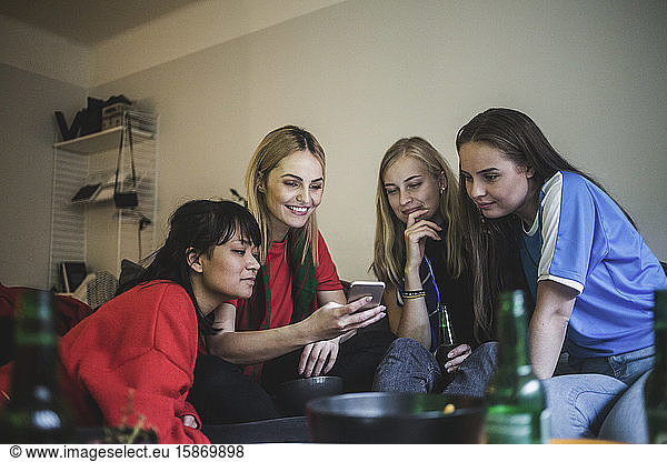 Smiling female friends using mobile phone while sitting at home
