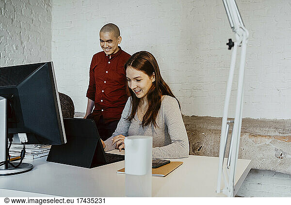 Smiling female hacker using laptop while working with colleagues at startup company