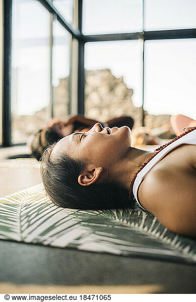 Smiling female instructor lying on exercise mat while doing yoga at retreat center