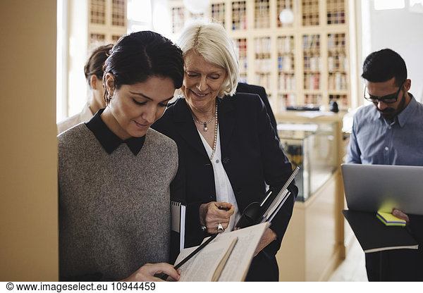 Smiling female lawyers discussing while walking with coworkers in library