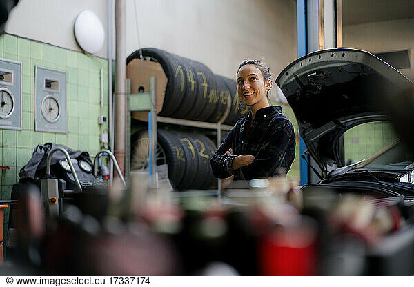 Smiling female mechanic with arms crossed looking away while leaning on car