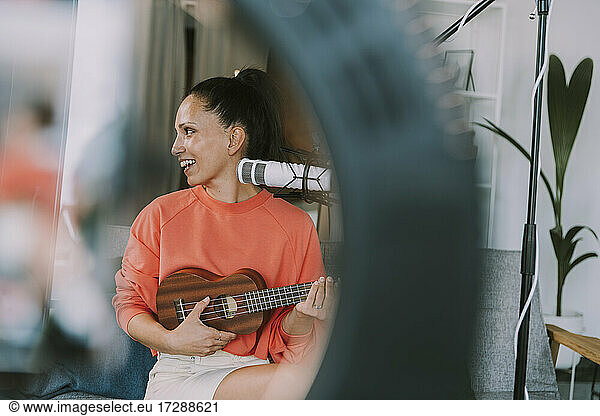 Smiling female musician looking away playing ukulele at home