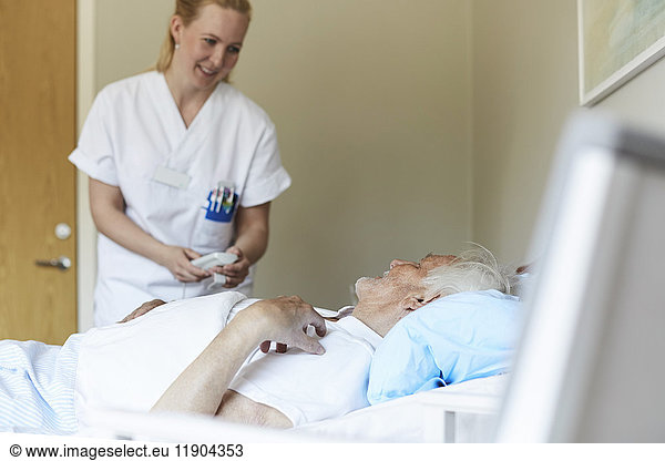 Smiling female nurse adjusting bed senior man's bed in hospital ward