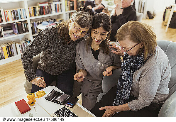 Smiling female nurse teaching laptop to elderly women at retirement home