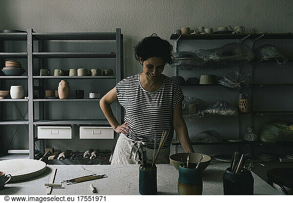 Smiling female owner looking at ceramics in workshop