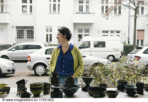 Smiling female owner looking away outside ceramics store