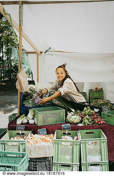Smiling female owner setting up vegetable stall at market