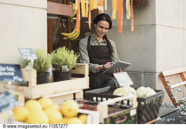 Smiling female owner using digital tablet while sitting at store entrance