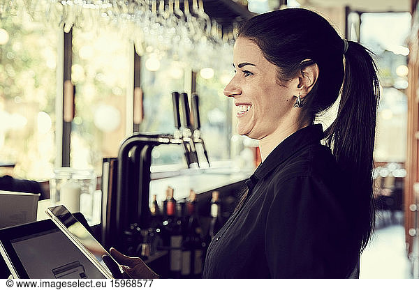 Smiling female owner with digital tablet looking away while standing in cafe