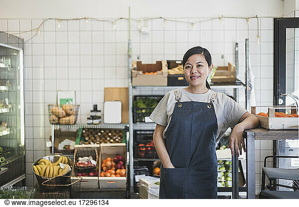 Smiling female owner with hand in pocket standing at store