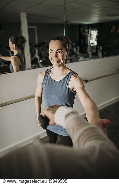 smiling female personal trainer coaches a person lifting weights