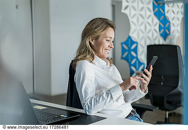 Smiling female professional using smart phone by desk at office