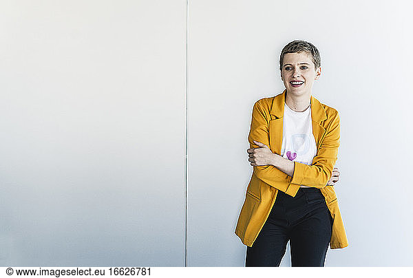 Smiling female professional wearing yellow blazer looking away while standing against wall in office