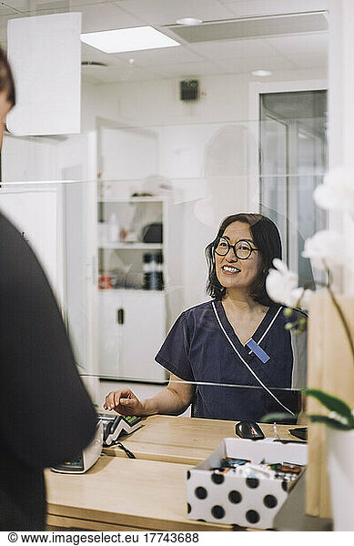 Smiling female receptionist wearing eyeglasses assisting patient at checkout in hospital